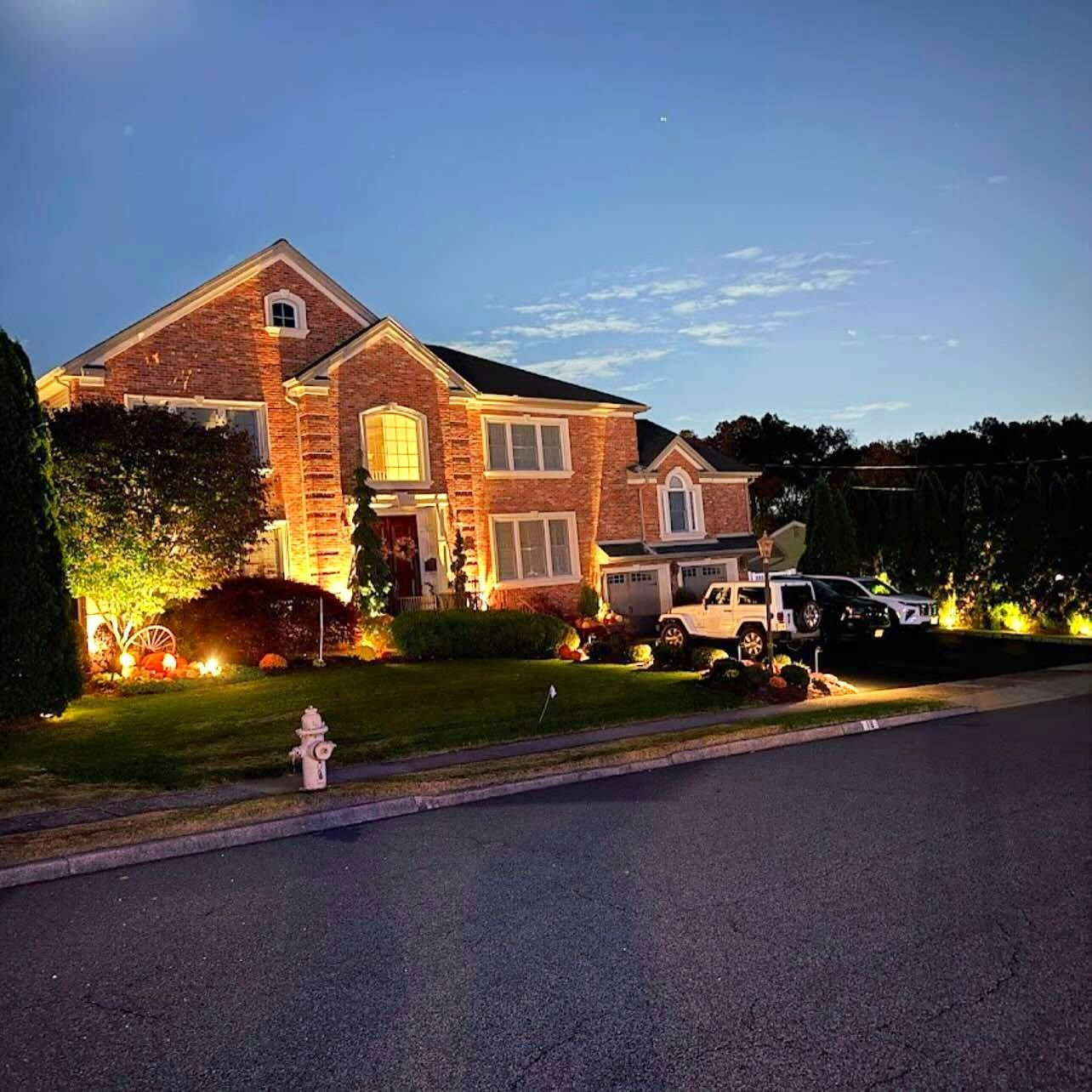 Brick colonial at dusk with warm uplights on the facade
