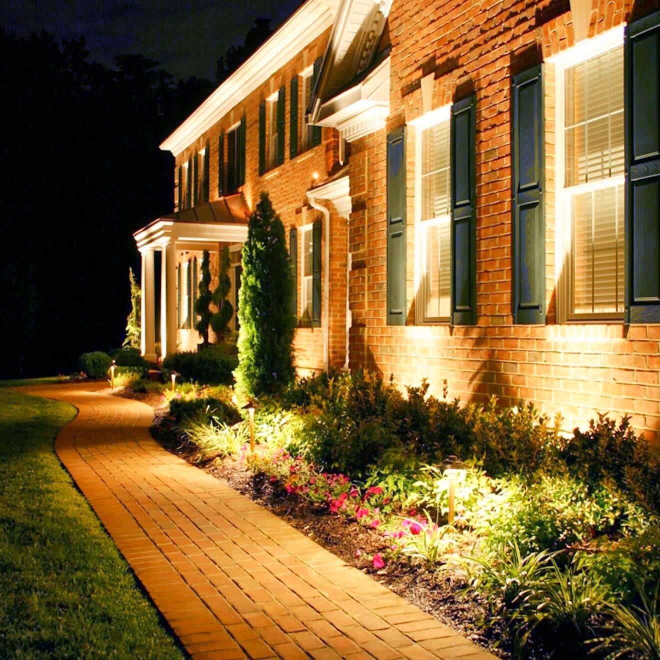 Brick colonial with uplights on the facade and path lights along the walkway