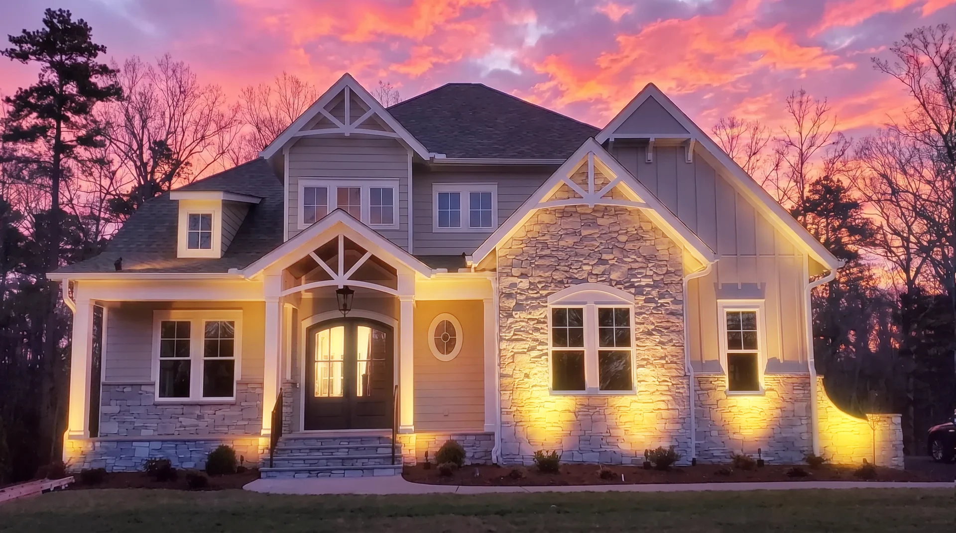 Two story home at sunset with warm white landscape uplights on the facade