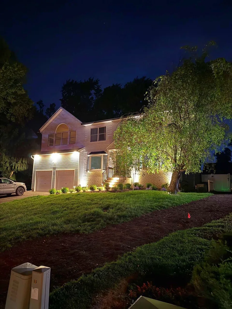 Two story home with facade uplights seen across the lawn