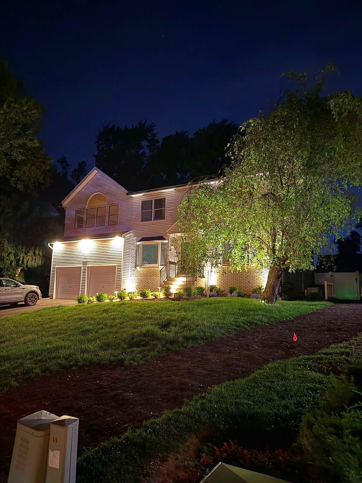 Two story home with facade uplights seen across the lawn